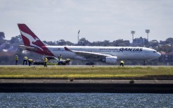 Workers check the runway as a Qantas plane prepares to take off behind them at Sydney International Airport. AFP/David Gray