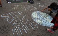 A person draws a message on a pavement calling for a stop to deep sea mining. Maylis Rolland/Hans Lucas via AFP