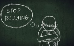 A young boy sitting on the floor with text reading stop bullying. GettyImages/asiandelight