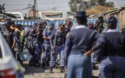 South African Police Service (SAPS) officers walk during raid to retrieve looted goods during a protest at Diepkloof Hostel in Soweto on May 19, 2025. 