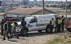 South African Police Service (SAPS) members and Gauteng Crime Prevention Wardens gather near the Forensic Pathology vehicle carrying the body of a person who died during a protest at Diepkloof Hostel in Soweto on May 19, 2025. 