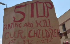 File: A protester holds a placard reading "Stop Raping and Kill(ing) our Children". AFP/Alexander Joe