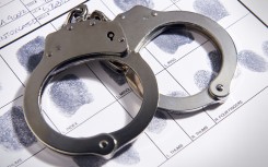 File: Handcuffs laying on top of fingerprint chart. GettyImages/TheCrimsonRibbon