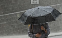File: A person uses an umbrella to shelter from the heavy rain. AFP/Peter Parks