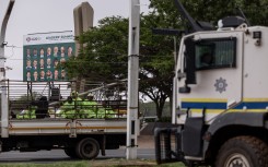 A truck transporting workers drives past a SAPS armoured vehicle outside the Nasrec Expo Centre in Johannesburg. AFP/Emmanuel Croset 