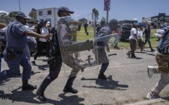 Riot police chase protesters from Dudula during a protest near the Nasrec Expo Centre. AFP/Ihsaan Haffejee