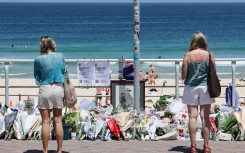 People stand in front floral tributes left at the promenade of Bondi Beach in Sydney. AFP/David Gray
