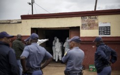 Police officers watch as SAPS Forensic Pathology Services members work at the scene of the Bekkersdal tavern attack. AFP/Emmanuel Croset