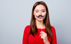 File: A woman holding a paper moustache. GettyImages/Deagreez