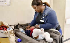 Baby with two casts on their legs being attended by a nurse