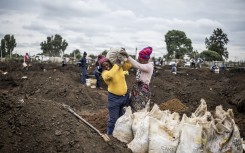 A woman grimaces as she is helped to load a sack of soil on her shoulder in a patch of land where artisanal miners look for gold outside Springs, Ekurhuleni, on February 15, 2026.