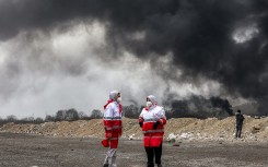 Members of Iran's Red Crescent society stand near smoke plumes from an ongoing fire following an overnight airstrike on the Shahran oil refinery in northwestern Tehran. AFP