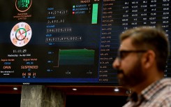A stockbroker walks past share prices on a digital board during a trading session at the Pakistan Stock Exchange. AFP/Rizwan Tabassum