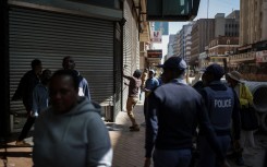 South African Police Service (SAPS) officers watch as a worker closes the shutters of a shop while protestors pass by during a protest march against undocumented migrants organised by “March and March” in Johannesburg on April 29, 2026. 