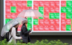 Pedestrians walk past an electronic quotation board displaying the Nikkei 225 stock prices. AFP/Kazuhiro Nogi