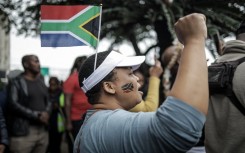 A protester gestures while wearing a South African flag over her head during a demonstration by the "March and March" movement. AFP/Rajesh Jantilal