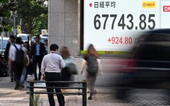 Pedestrians pass by a stock price indicator flashing its closing rate. AFP/Toshifumi Kitamura