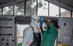 A hygiene worker helps a doctor put on personal protective equipment (PPE) before entering the Rwampara Ebola Treatment Centre. AFP/Benediction Murhabazi