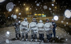Police officers guard a Diarco supermarket under falling snow after an attempted looting
