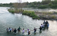 A group of migrants hold hands as they cross the Rio Grande river