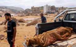 People walk past the body of a victim from the flood which devastated Derna, eastern Libya