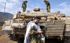 An Israeli soldier prays in front of a Merkava tank near the the northern town of Kiryat Shmona, close to the border with Lebanon, on October 8, 2023
