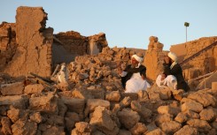Afghan men sit in the rubble of their flattened homes in Sarbuland village in Herat province following Saturday's earthquake