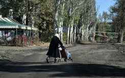 An elderly woman carries bottles of water in a child stroller down a street in the frontline town of Chasiv Yar in eastern Ukraine