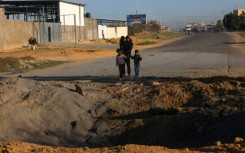 Palestinians fleeing Khan Yunis in the southern Gaza Strip further south toward Rafah stare at a bomb crater in the Salah Al-Din road