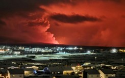 Houses in Iceland's Hafnarfjordur are seen as smoke billows in the distance, the night sky turned orange by lava from an volcanic eruption