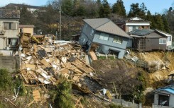 Damaged houses, including one totally collapsed (C), are pictured along a street in Wajima, Japan