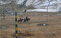 A guide leads horses along a path near ski slopes usually covered in snow in Gulmarg 