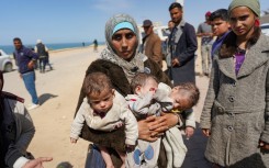 A woman carries three babies in the central part of the Gaza Strip after fleeing the Al-Shifa hospital compound in Gaza City on Thursday