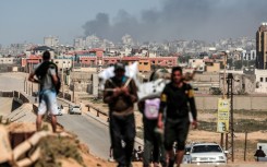 People flee as smoke rises above buildings near the Al-Shifa hospital compound during Israeli bombardment in Gaza City on March 21, 2024