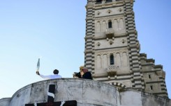 Basile Boli holds the Olympic torch aloft in front of the basilica of Notre-Dame de la Garde in Marseille