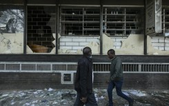 Pedestrians walk past damaged shops vandalised  during the deadly violence which rocked Nairobi over proposed tax hikes