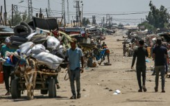 An Israeli tank takes position in the background as displaced Palestinians flee the Shakush area on the northwestern outskirts of Rafah, southern Gaza