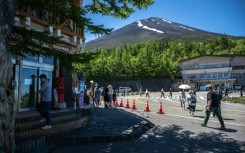 The summit of Mount Fuji is seen as people gather in front of the restaurant and shopping area of the Fuji Subaru Line 5th station, which leads to the popular Yoshida trail for hikers -- new rules will be in effect this season to combat overcrowding