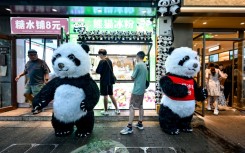 Men wearing panda costumes stand outside food stalls in Beijing in July 2024