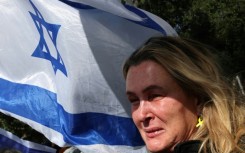 An onlooker holding an Israeli flag cries as a convoy transporting the bodies of dead hostages arrives in Tel Aviv on Thursday