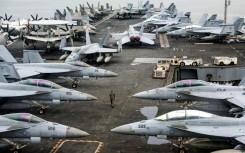 A US Navy officer walks past fighter jets parked on the flight deck of the USS Abraham aircraft carrier