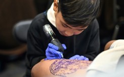 Wielding a cumbersome tattoo gun, nine-year-old Napat Mitmakorn inks the pattern of a fanged serpent on a man's upper thigh