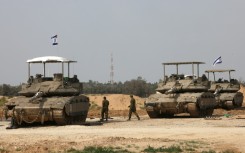 Israeli army soldiers walk past tanks at a position near Israel's southern border with the Gaza Strip
