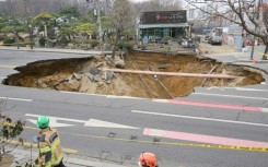 Rescue workers walk past a sinkhole outside a plant shop on a road in Seoul