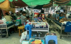 Hundreds of patients, including babies, the elderly and Buddhist monks, lie on gurneys in a hospital car park in the sweltering heat of Mandalay