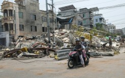People ride a motorbike past damaged buildings in Mandalay, Myanmar