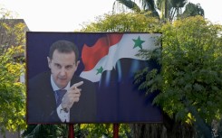 A portrait of ousted Syrian president Bashar al-Assad next to a national flag is slightly damaged by shrapnel outside the Barzeh scientific research centre north of the Syrian capital Damascus, after being targeted by a December 2024 Israeli airstrike