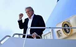 US President Donald Trump raises a fist as he steps off Air Force One at Palm Beach International Airport in Florida on April 11, 2025, while heading to spend the weekend at his Mar-a-Lago resort