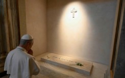 Vatican News published a photo of the white-robed pope kneeling before Francis's simple marble tomb