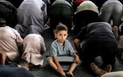 A boy looks on as he sits between Muslim worshippers prostrating as they perform the early morning prayers for Eid al-Adha